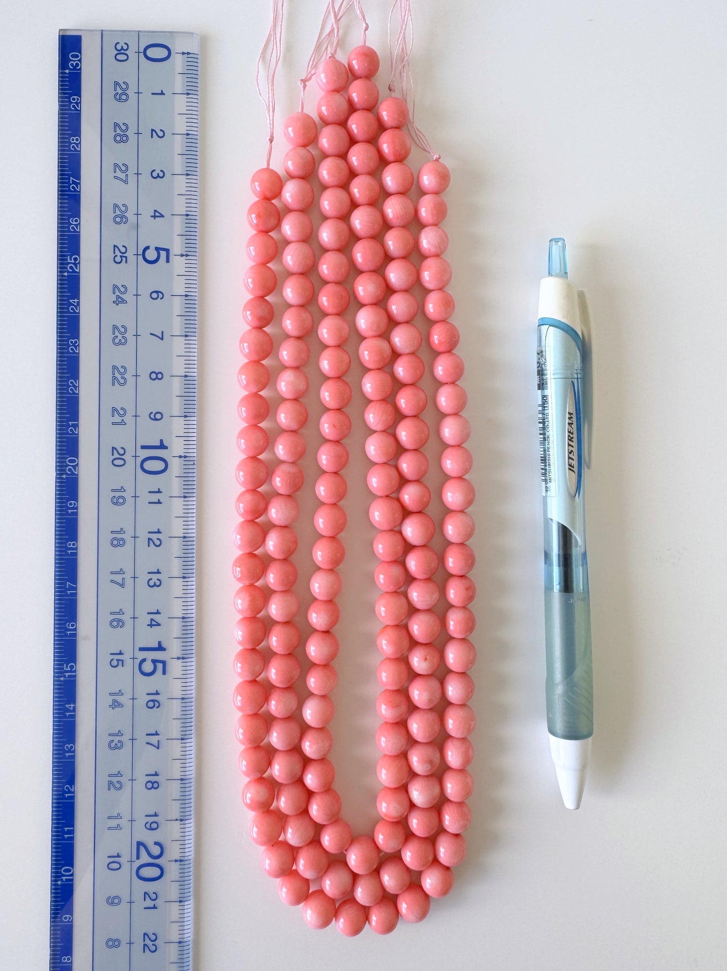 a collection of pink beads and a pen, arranged on a white surface.