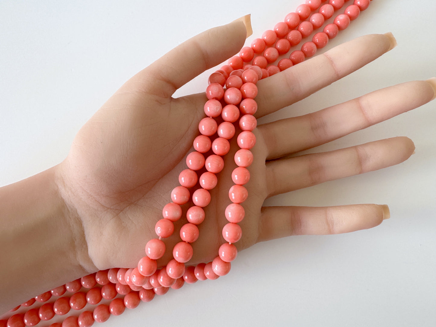 A hand holding a string of coral-colored beads.