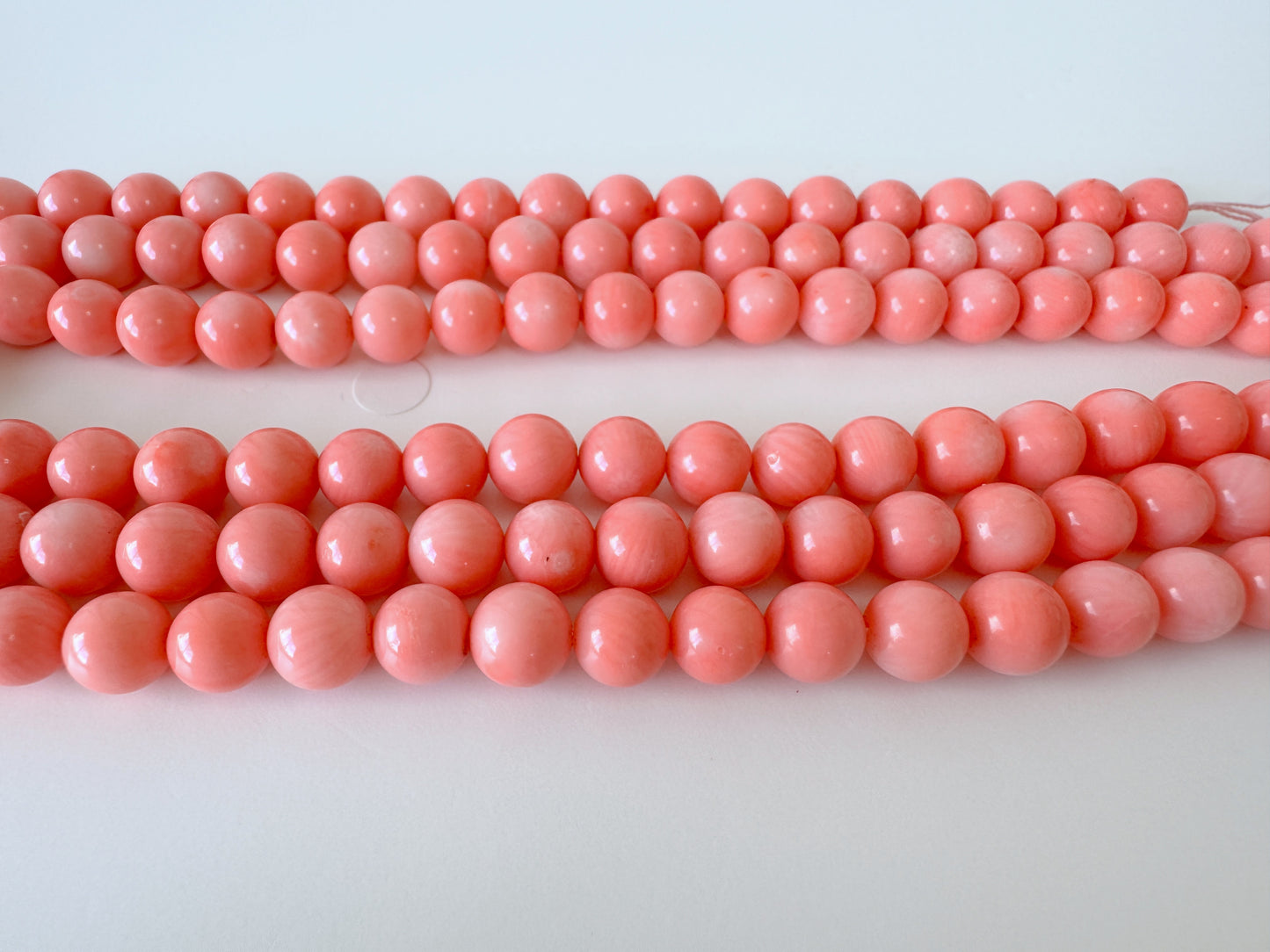 A collection of numerous bright pink coral beads arranged in rows on a white background.