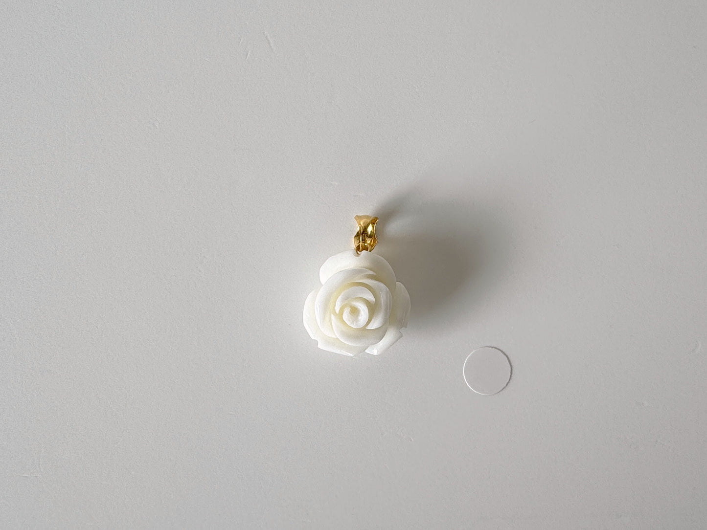 A white rose-shaped pendant with a gold clasp is displayed against a plain white background.
