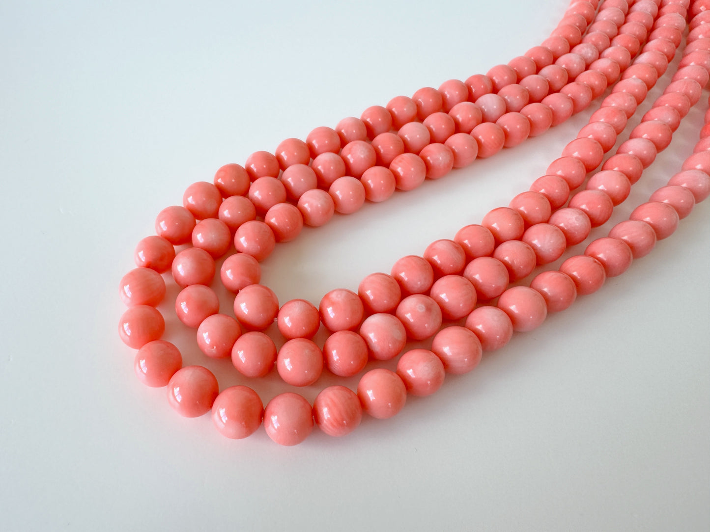 A collection of pink coral beads arranged in a curved pattern on a white background.