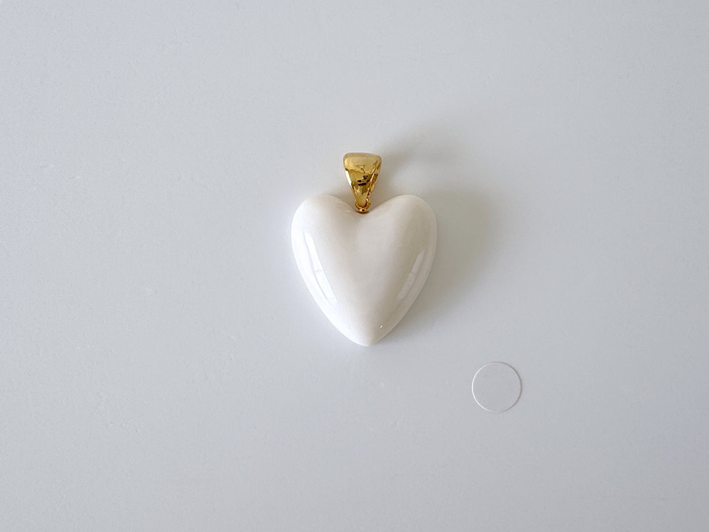 A white heart-shaped pendant with a gold clasp is displayed against a plain white background.