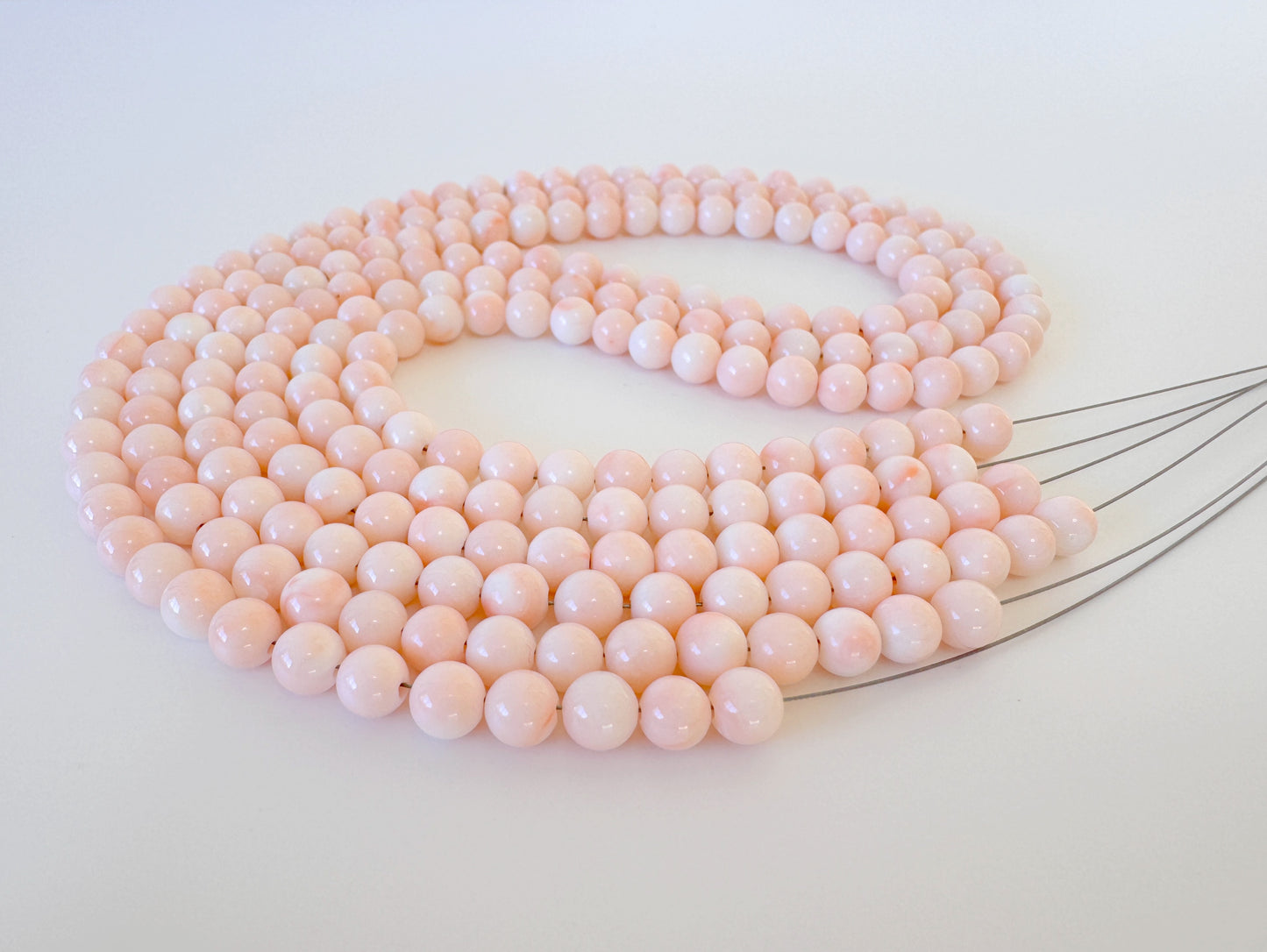 A large, intricate necklace composed of numerous small, round beads in a soft, pastel pink color.