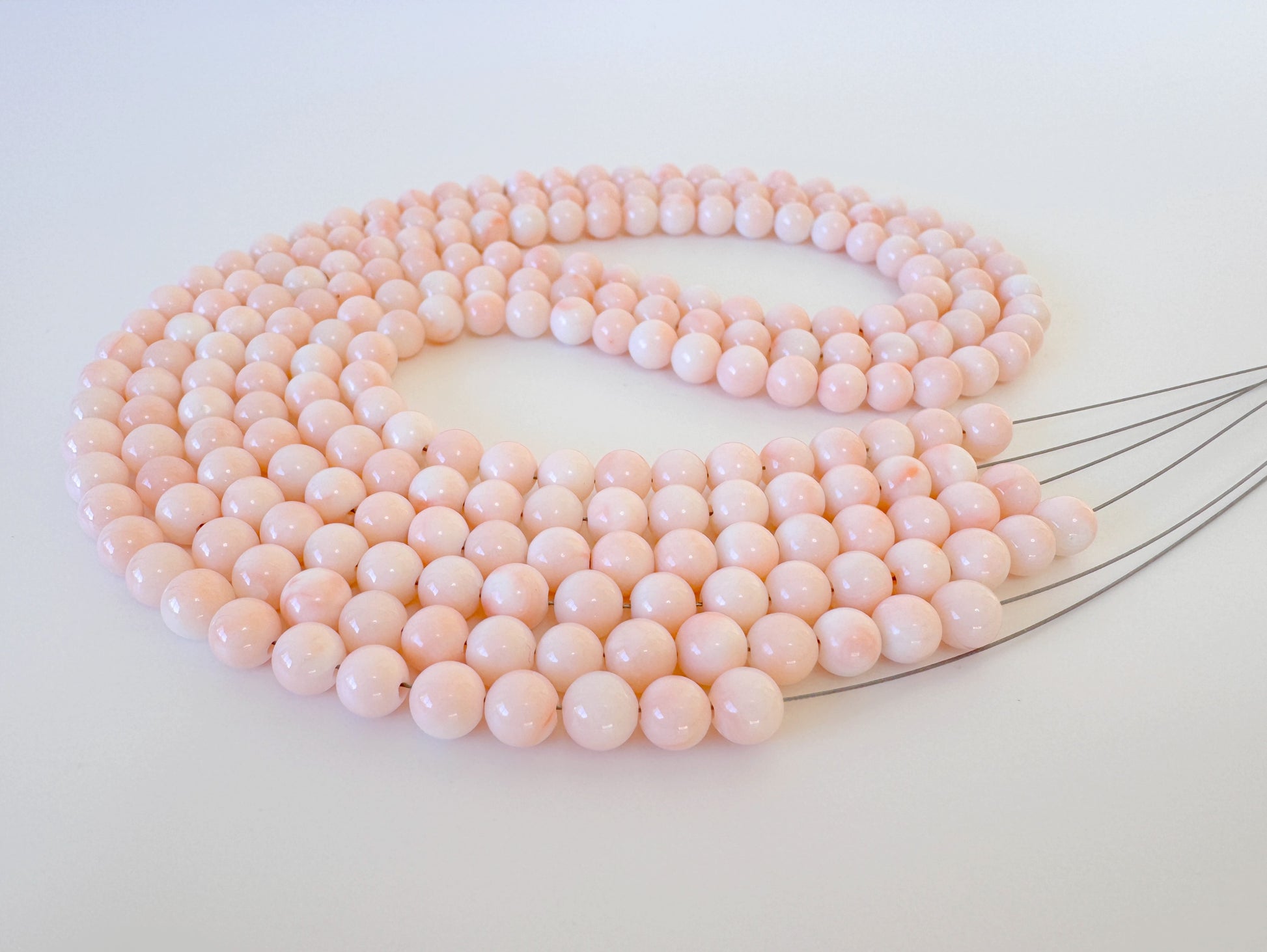 A large, intricate necklace composed of numerous small, round beads in a soft, pastel pink color.
