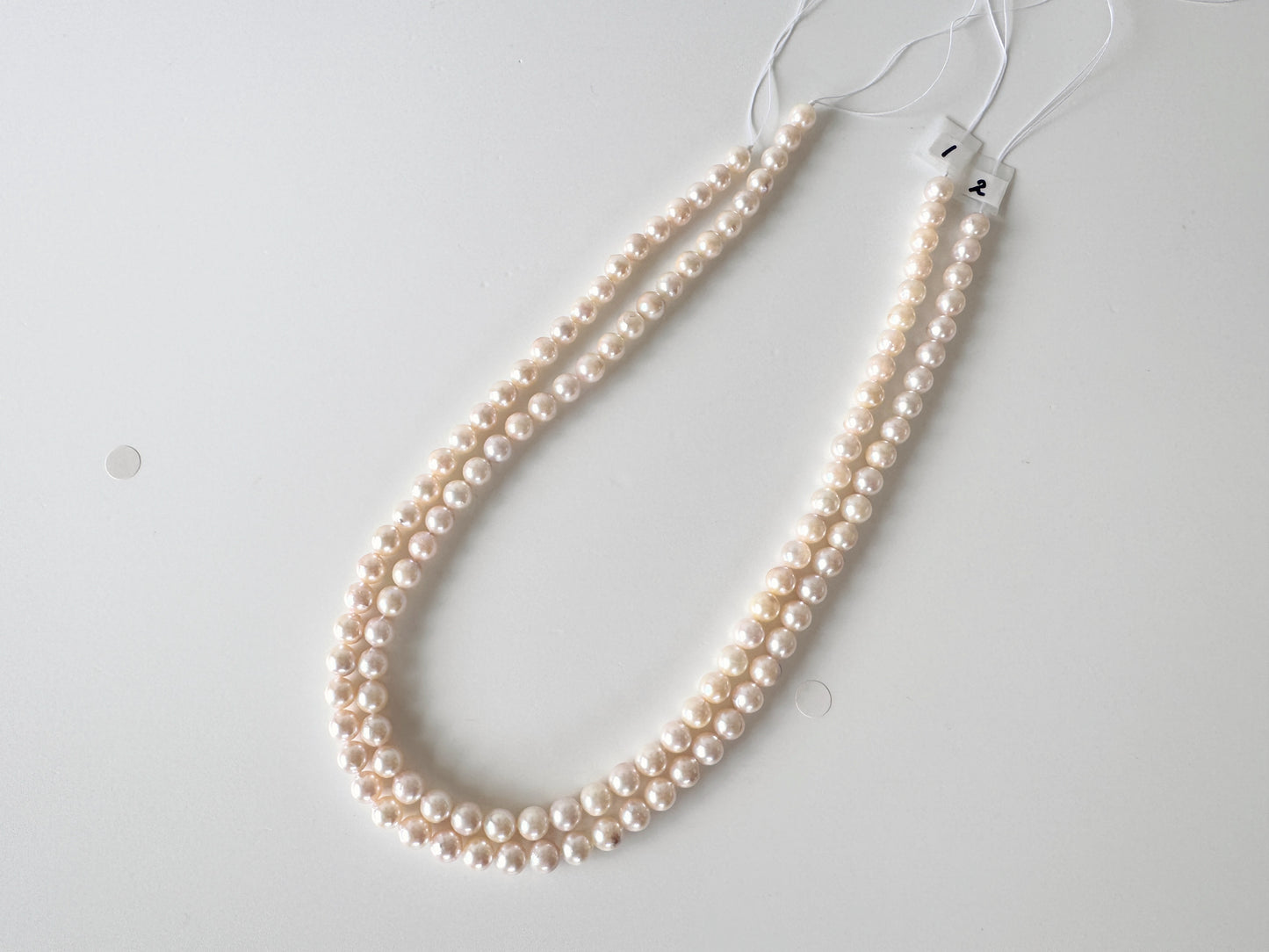A necklace made of small, round, white pearls is displayed on a white surface.