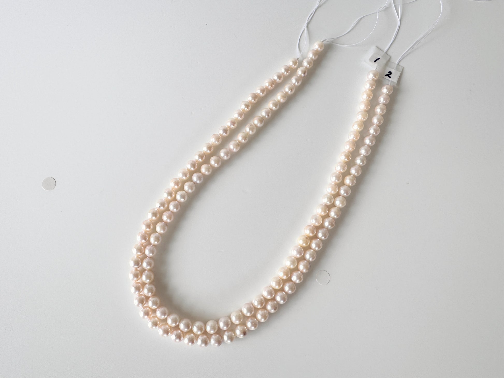 A necklace made of small, round, white pearls is displayed on a white surface.