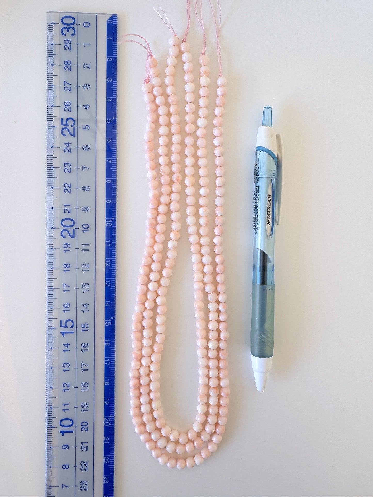 a collection of items, including a ruler, a pen, and several beads, arranged on a white surface.