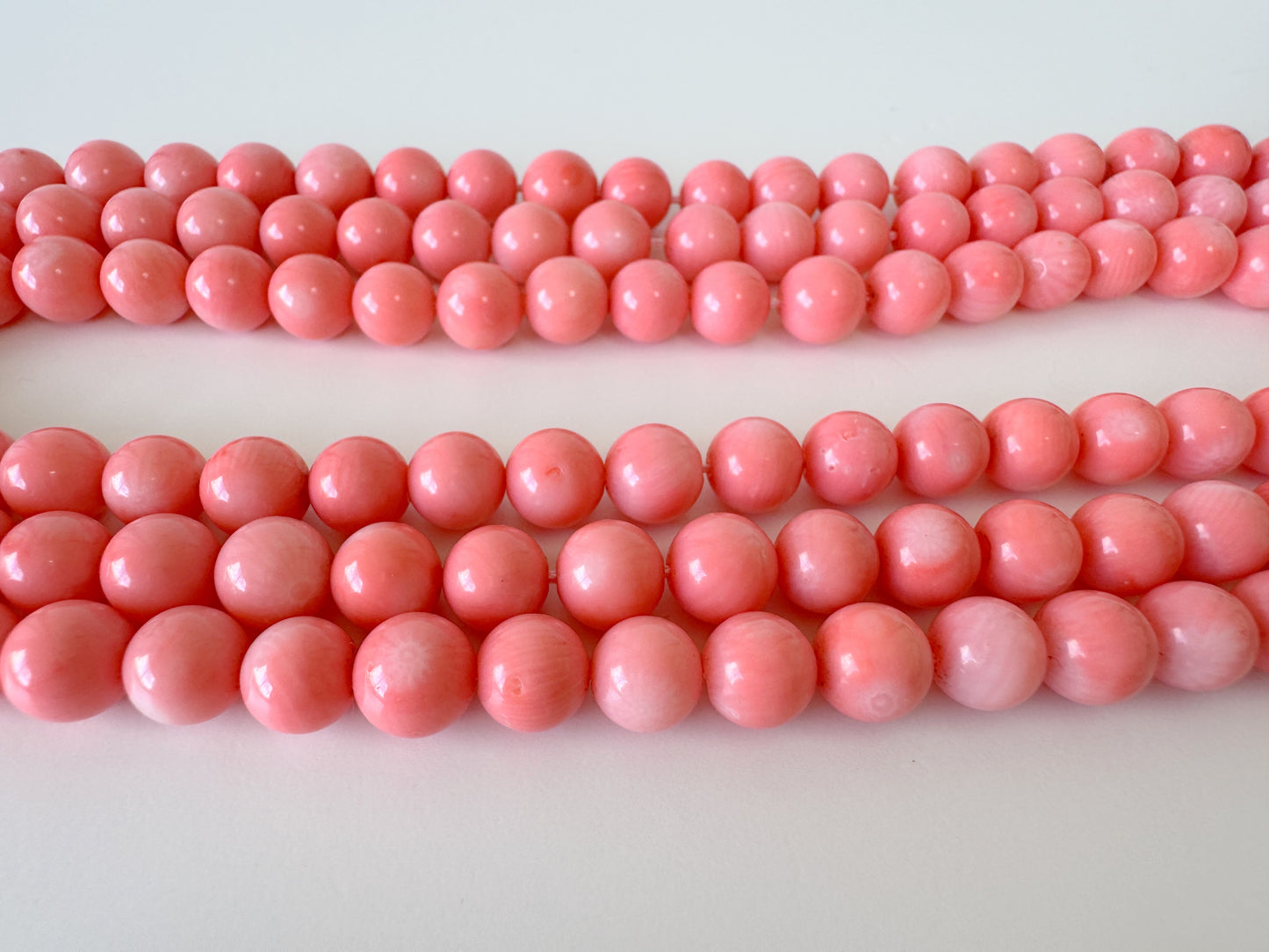 A collection of pink coral beads arranged in rows on a white background.