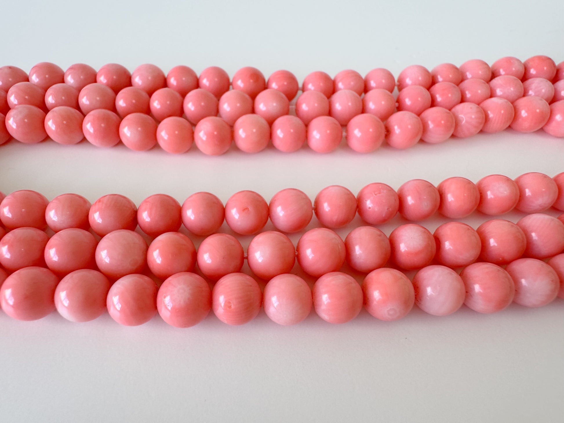 A collection of pink coral beads arranged in rows on a white background.
