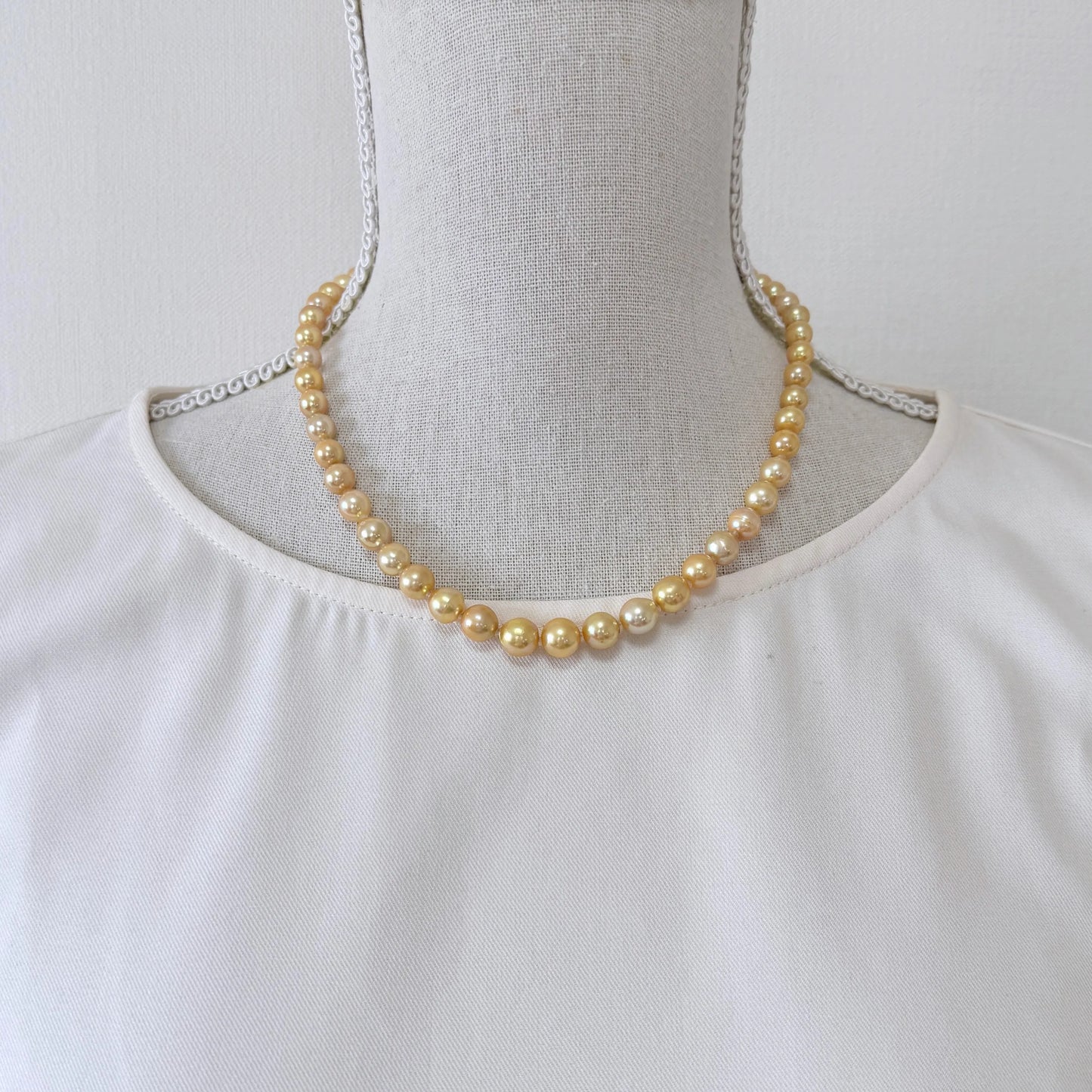 A mannequin wearing a white blouse with a gold pearl necklace.