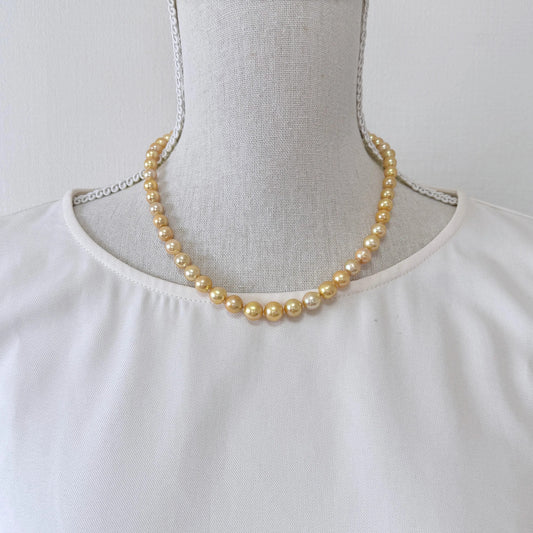 A mannequin wearing a white blouse with a gold pearl necklace.