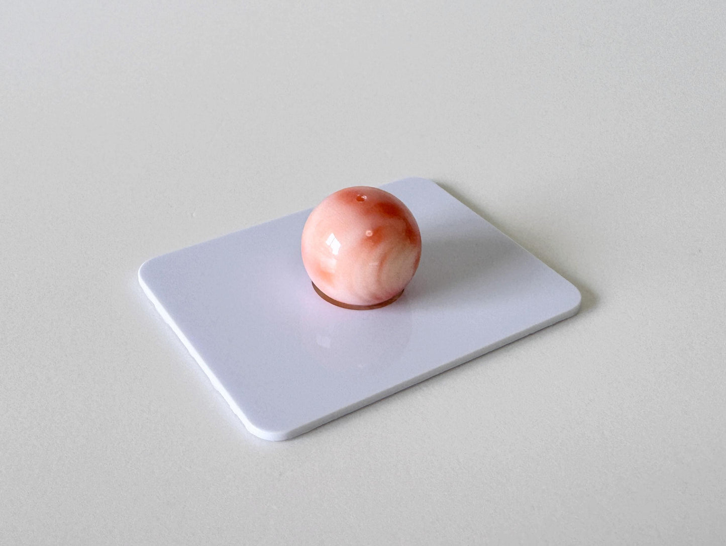 A single, round, pink object is centered on a white surface.