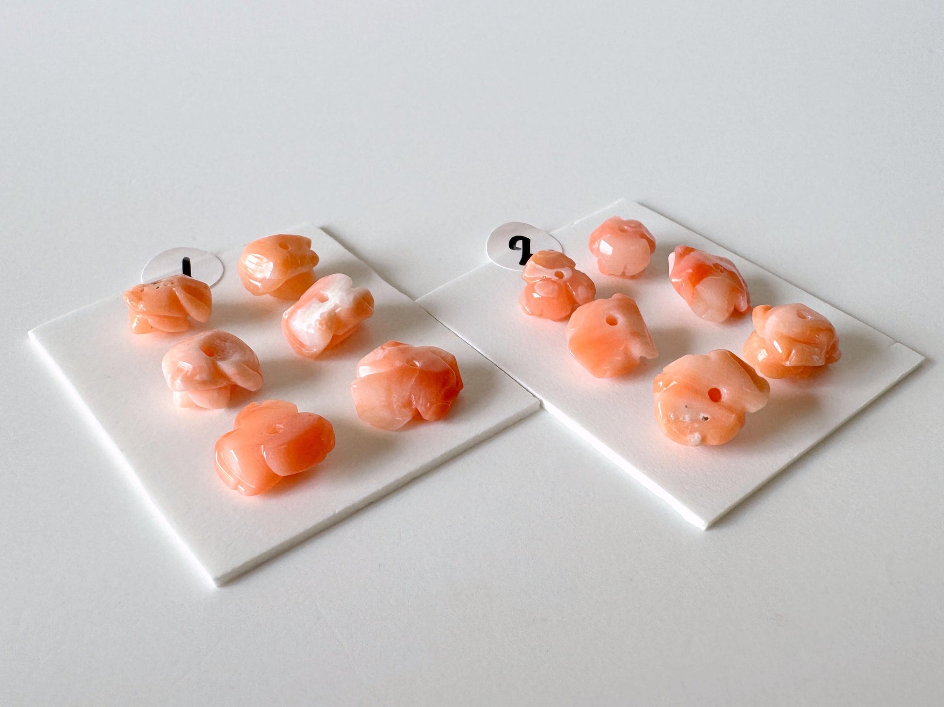 two white plates with small orange objects, possibly beads or candies, arranged on a white surface.