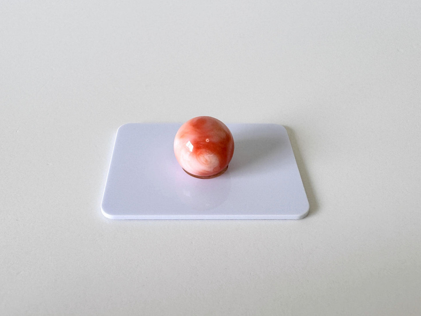 A single, round, red and white object is centered on a white surface.