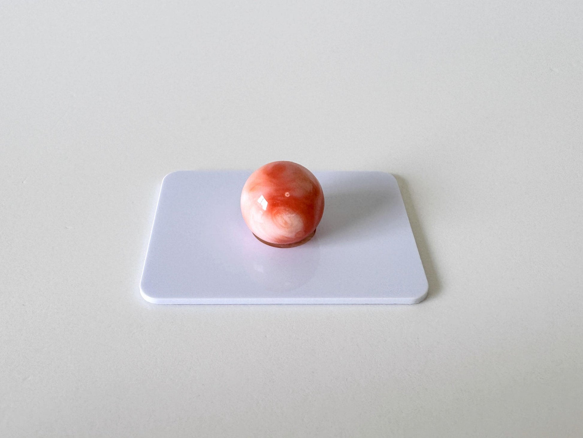 A single, round, red and white object is centered on a white surface.