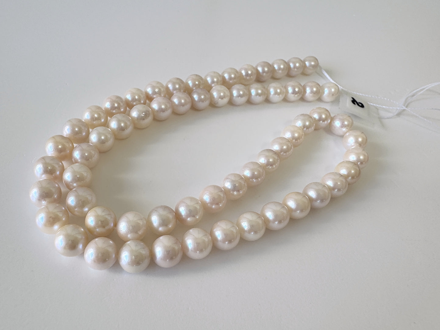 A pair of long, white pearls lying on a white surface.