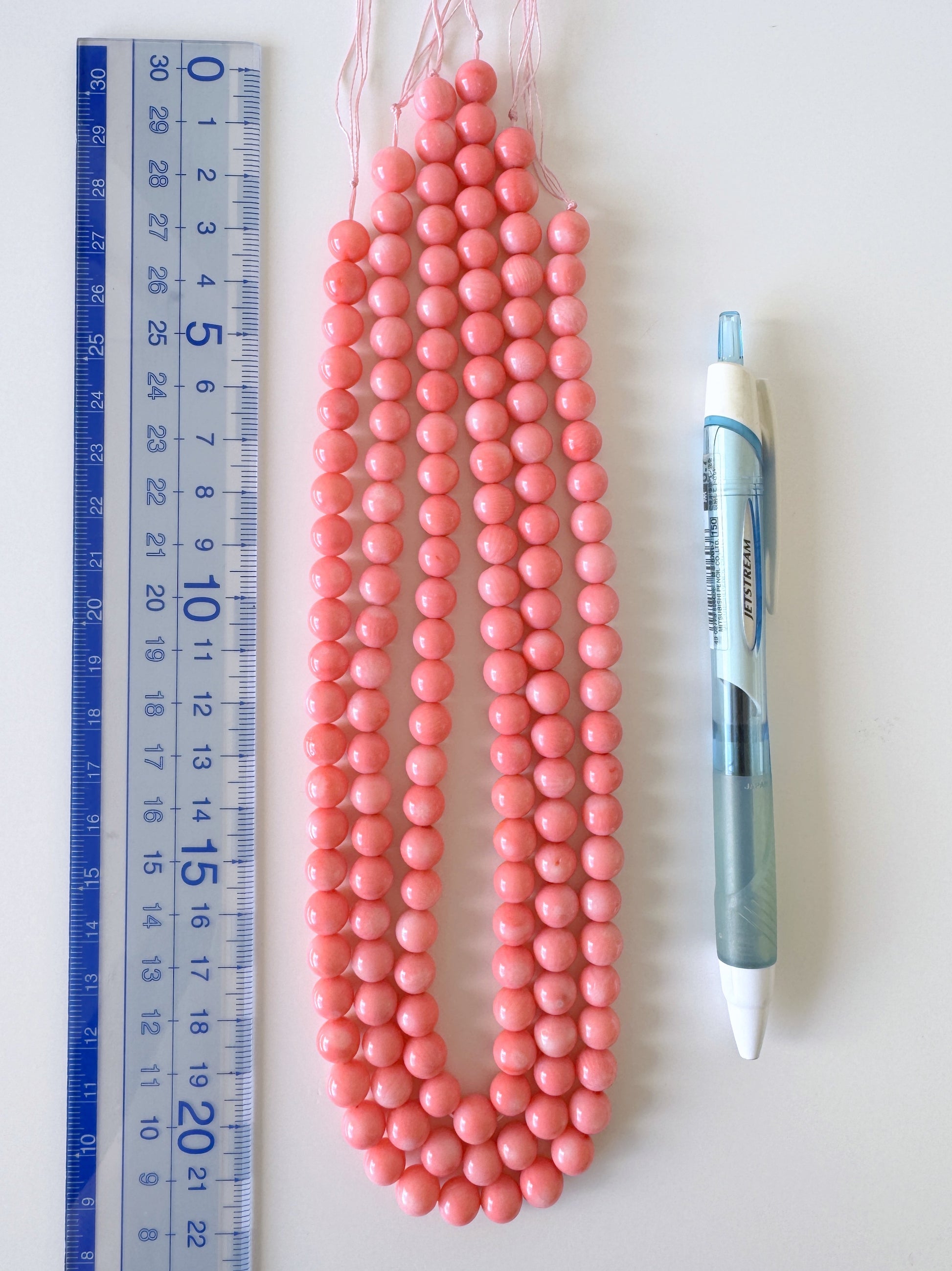 a collection of pink beads and a pen, arranged on a white surface.