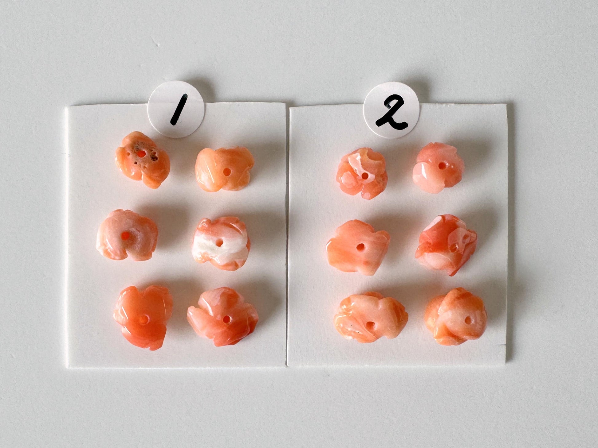 a collection of small, orange-colored objects arranged on two white papers, with each paper having a number and a small black circle with a number inside.