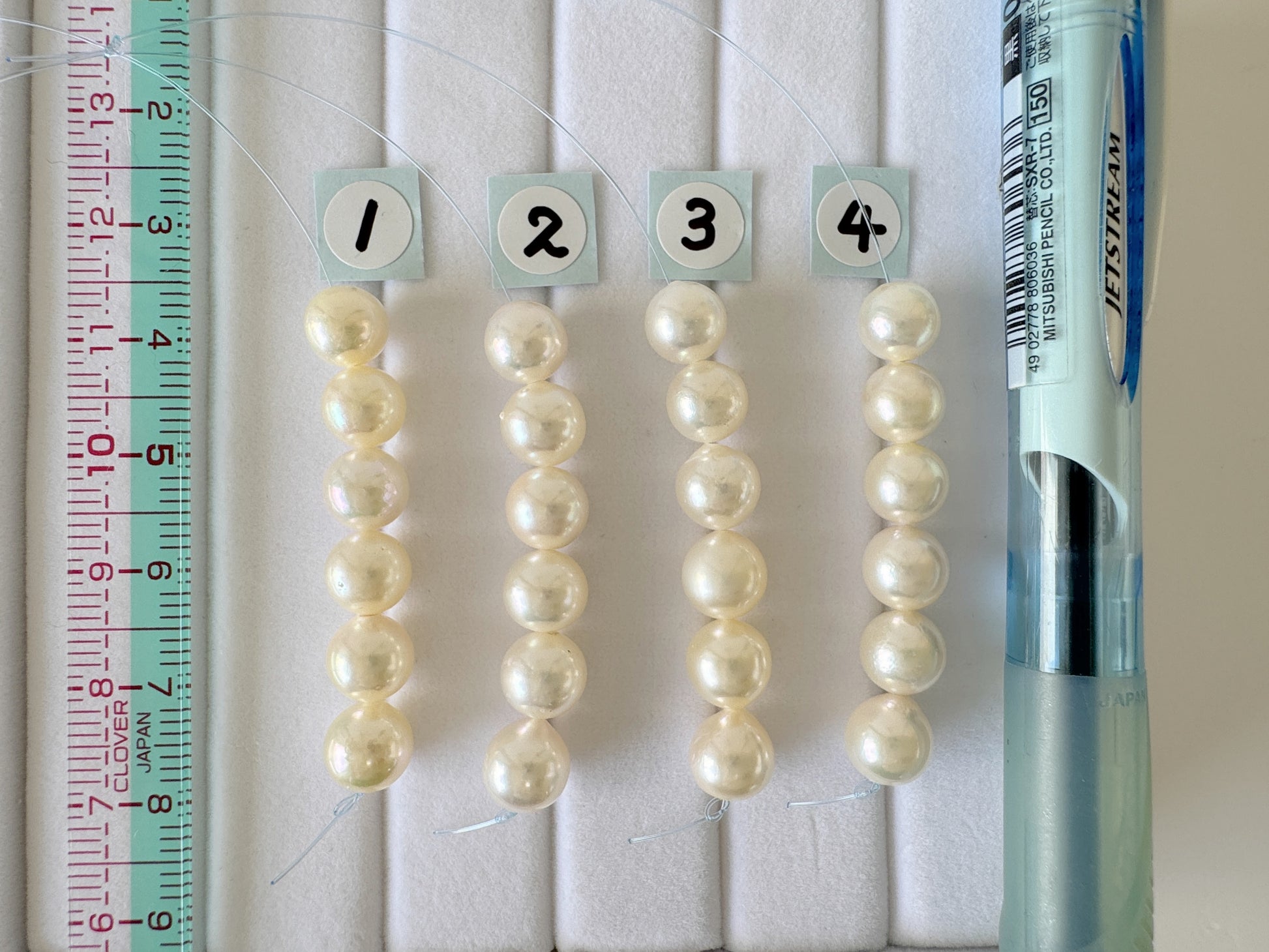 four rows of white pearls, each row numbered 1 through 4, with a ruler and a pen on the right side.