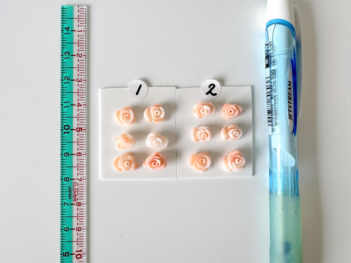a collection of small pink rose-shaped objects, a blue pen, and a ruler, all placed on a white surface.