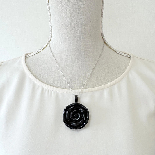 A mannequin wearing a white blouse and a black pendant necklace with a black rose design.