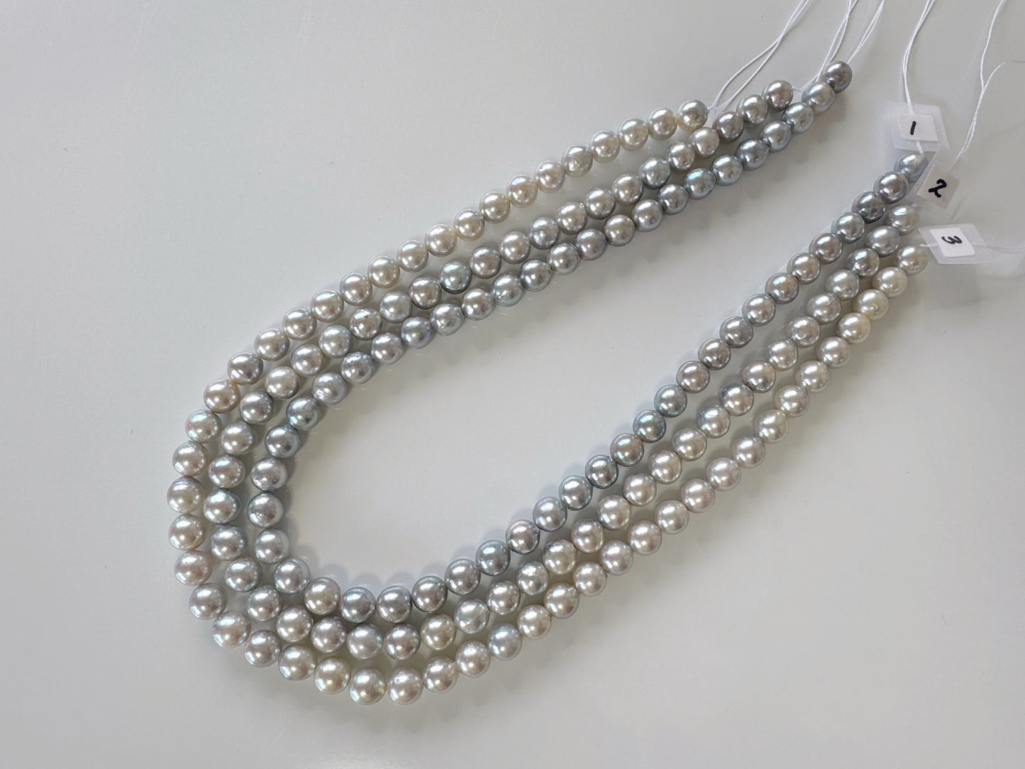 A collection of pearl necklaces with various shades of gray and white pearls arranged in a row.