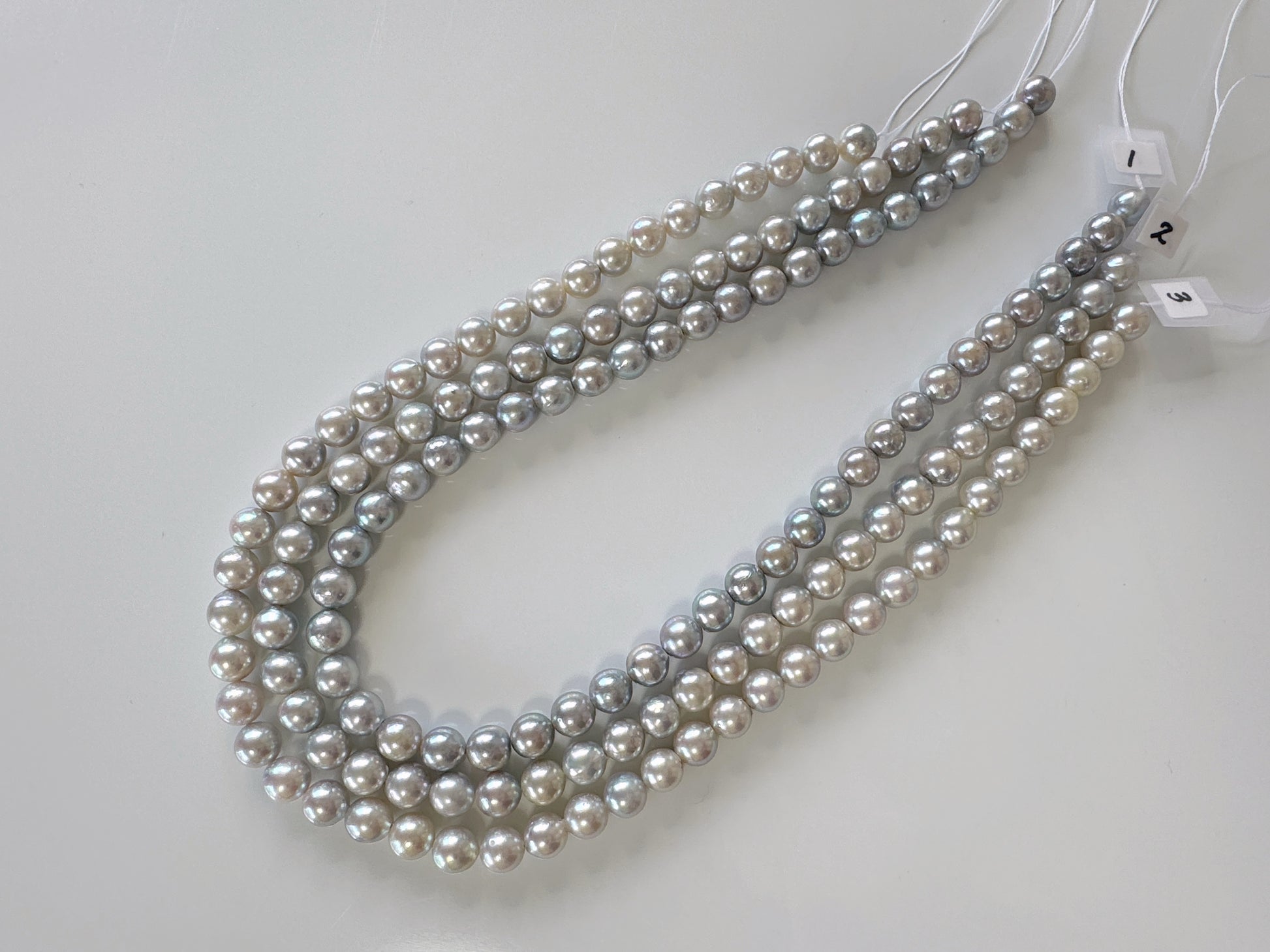 A collection of pearl necklaces with various shades of gray and white pearls arranged in a row.