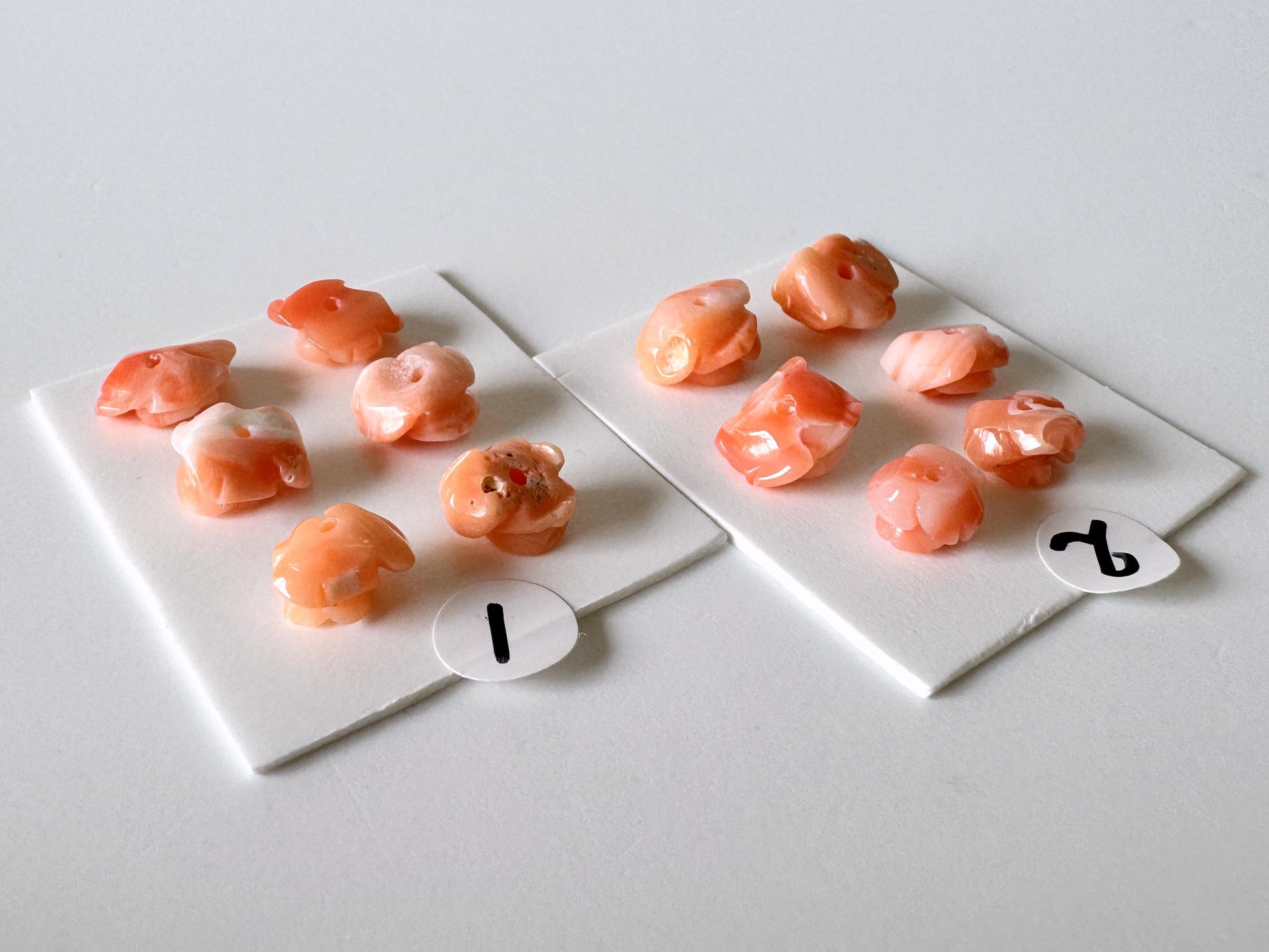 two white plates with small orange objects, possibly pearls or beads, placed on a white surface.
