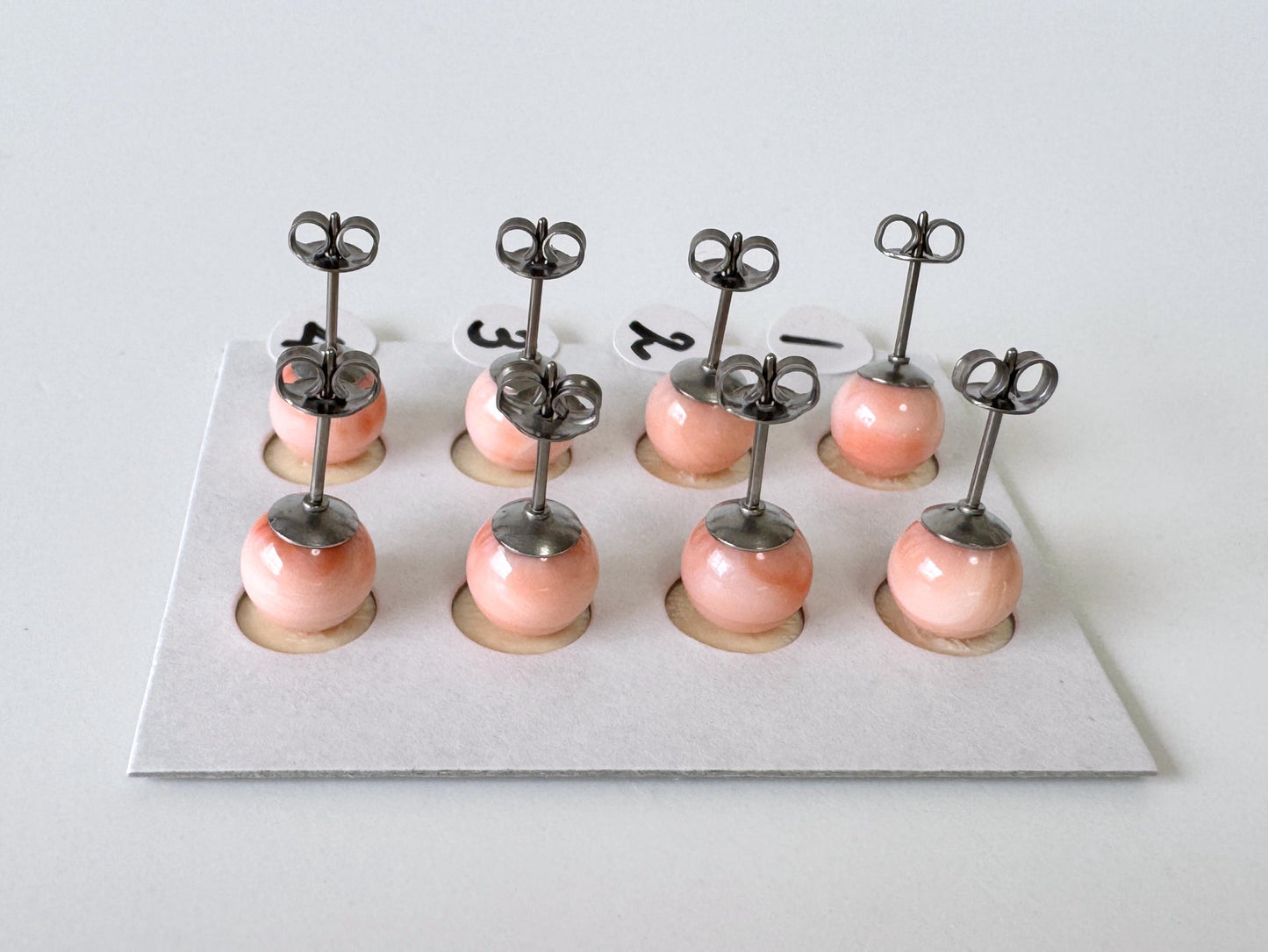 A group of nine small, round earrings with metal posts and round pendants, arranged in a grid-like pattern on a white surface.