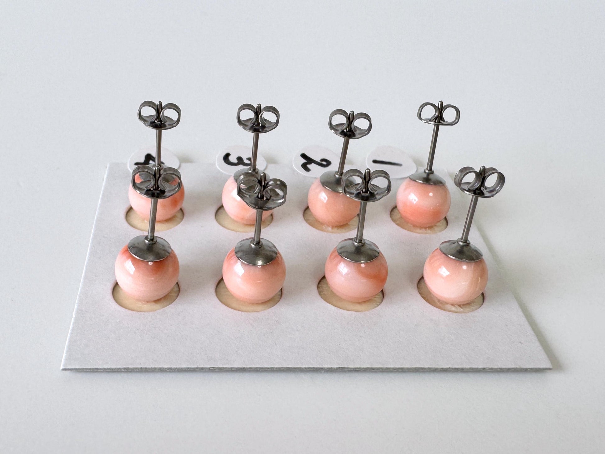 A group of nine small, round earrings with metal posts and round pendants, arranged in a grid-like pattern on a white surface.