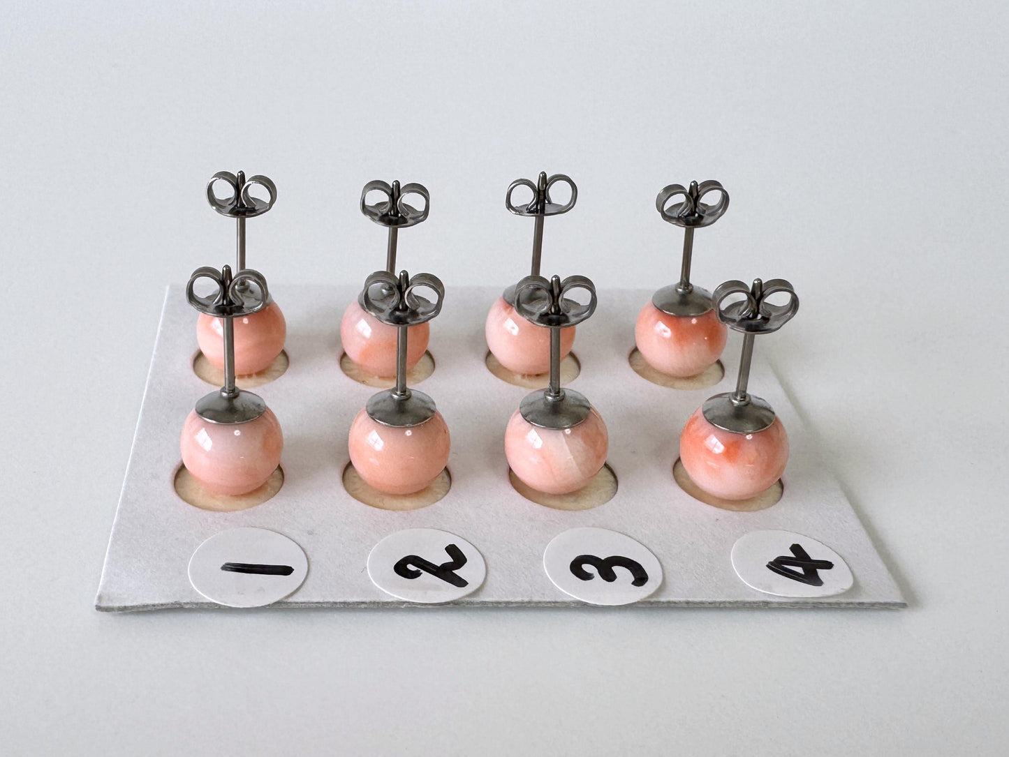 A group of nine small, round earrings with metal hooks, each with a small, round ball at the bottom. The earrings are arranged in a grid-like pattern on a white surface, with each pair labeled with a number from 1 to 4.