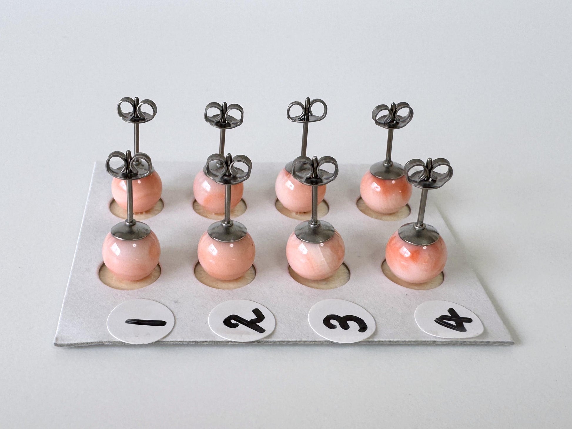 A group of nine small, round earrings with metal hooks, each with a small, round ball at the bottom. The earrings are arranged in a grid-like pattern on a white surface, with each pair labeled with a number from 1 to 4.