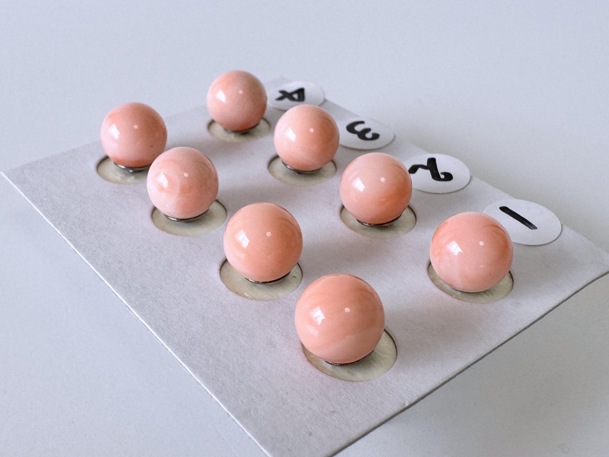 a group of small, round, pink beads arranged in a grid-like pattern on a white surface.