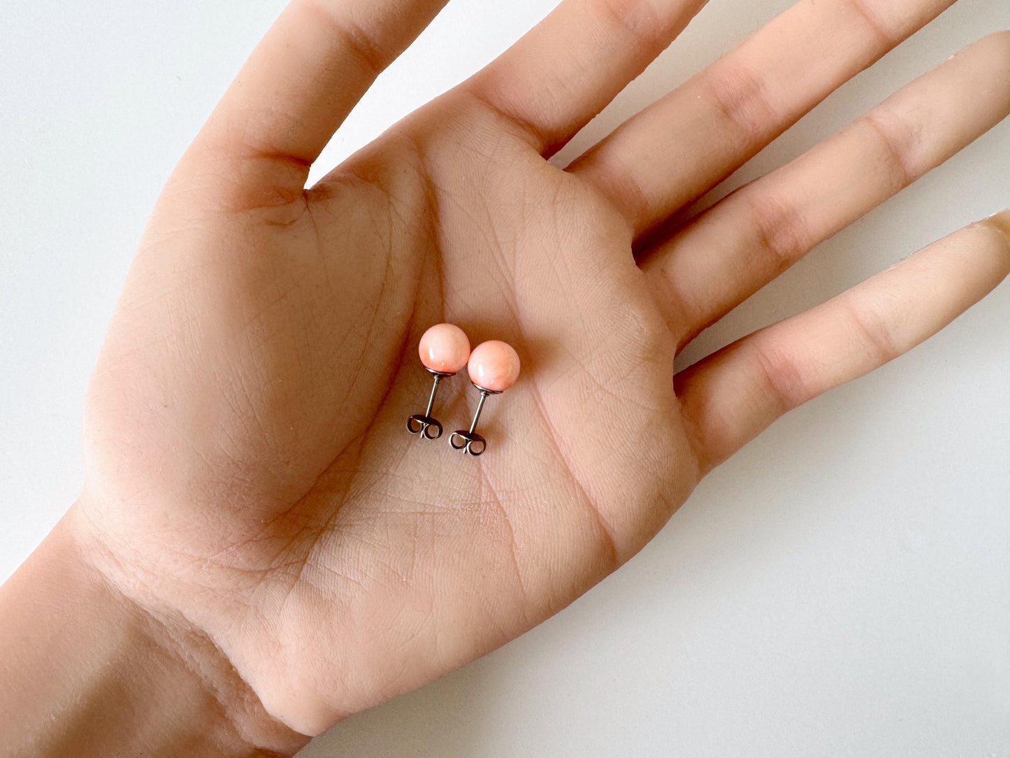 A hand holding a pair of small, round earrings with a light pink color.