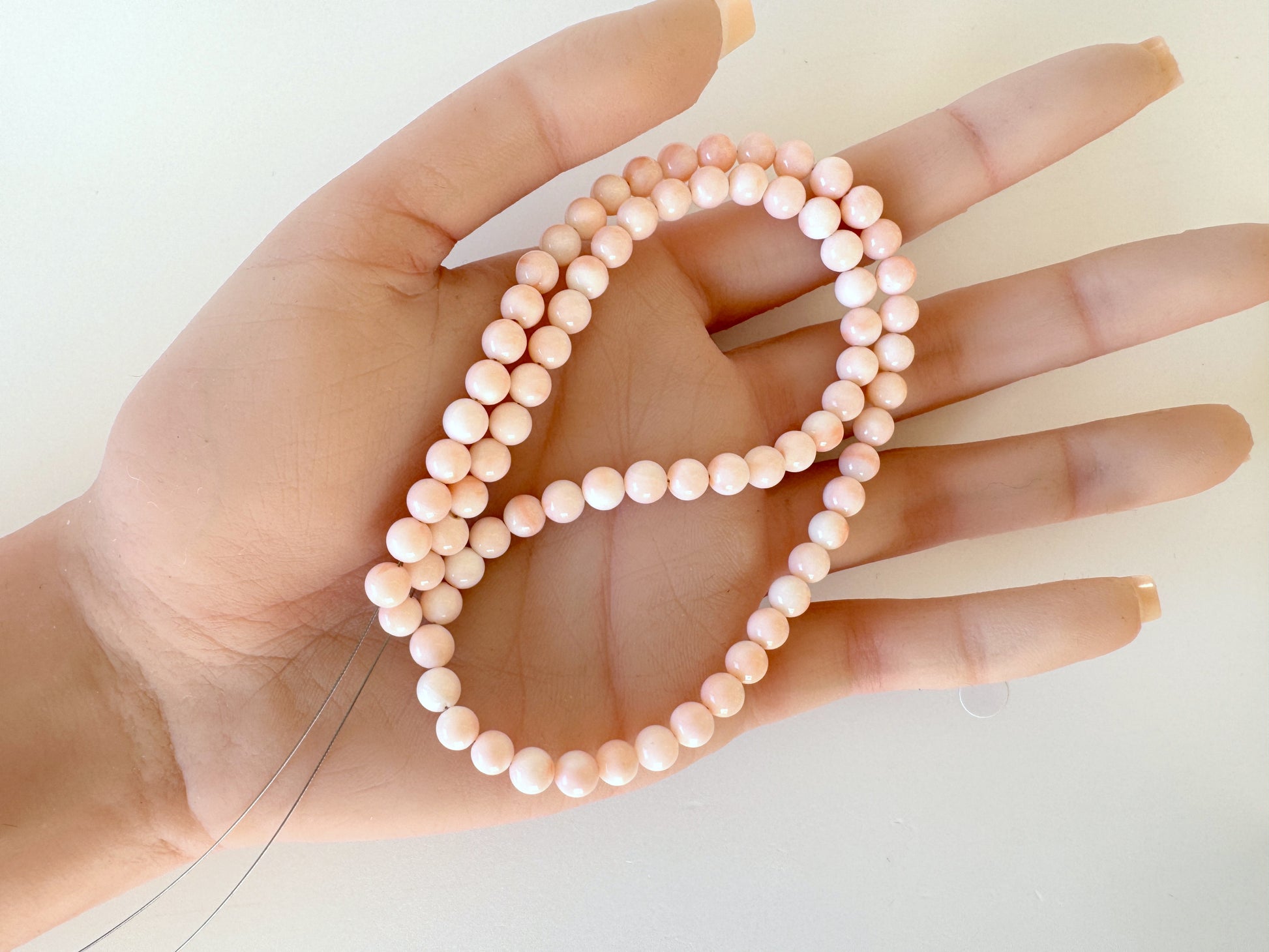 A hand holding a string of small, round, white pearls.