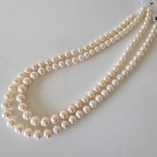 A necklace with three strands of white pearls is displayed on a white surface.