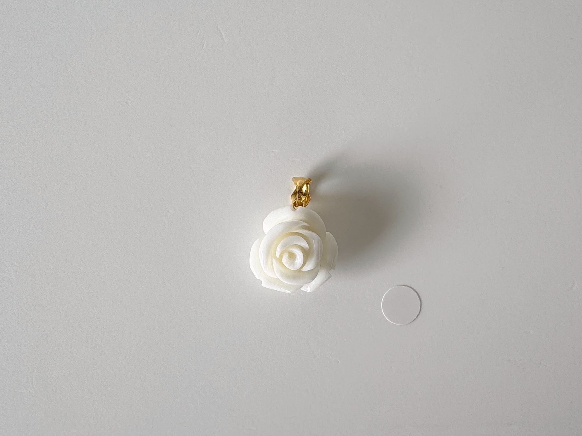 A white rose-shaped pendant with a gold clasp is displayed against a plain white background.