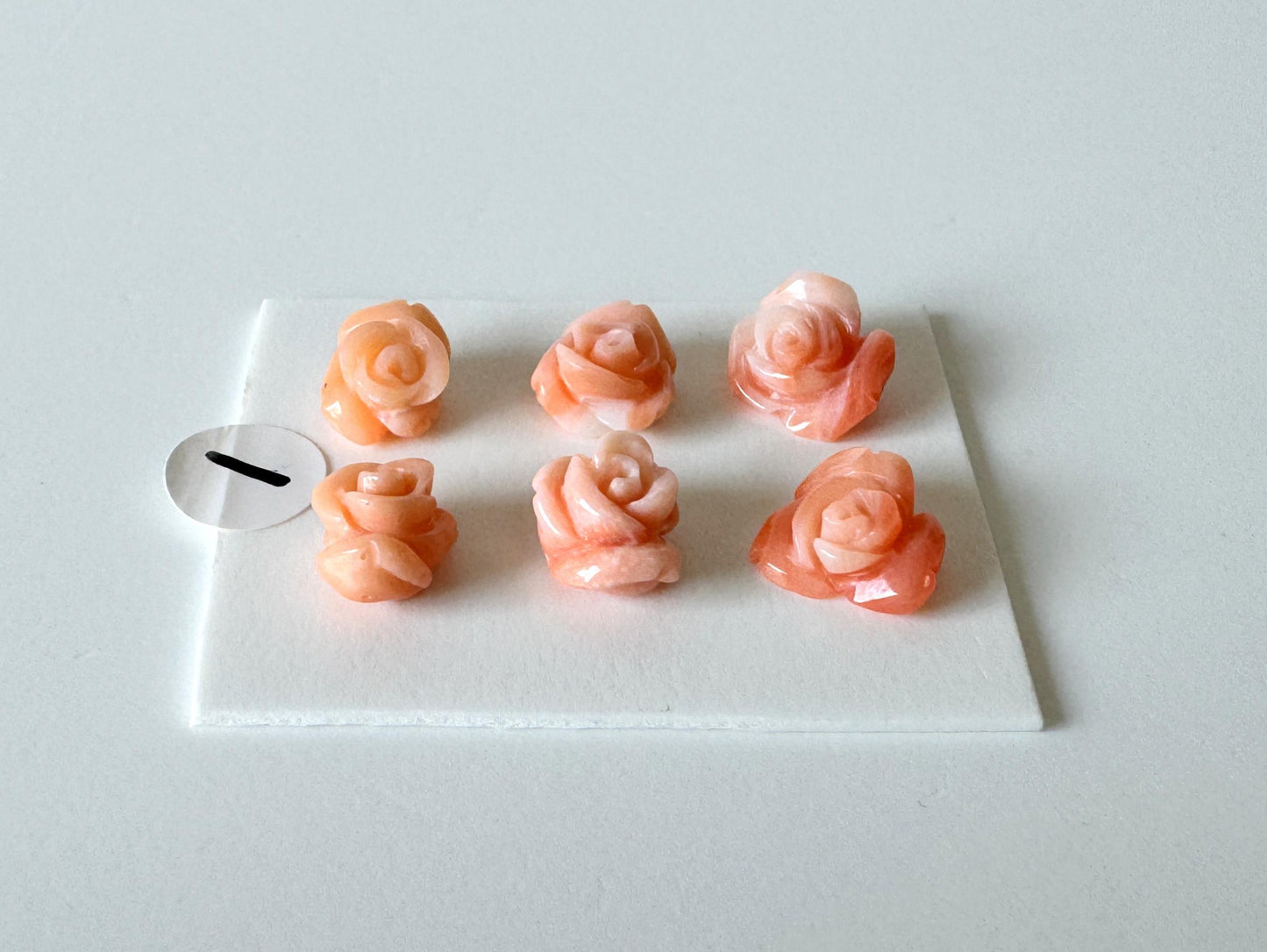 Six pink rose-shaped objects are arranged on a white surface, with one small white circle placed next to them.
