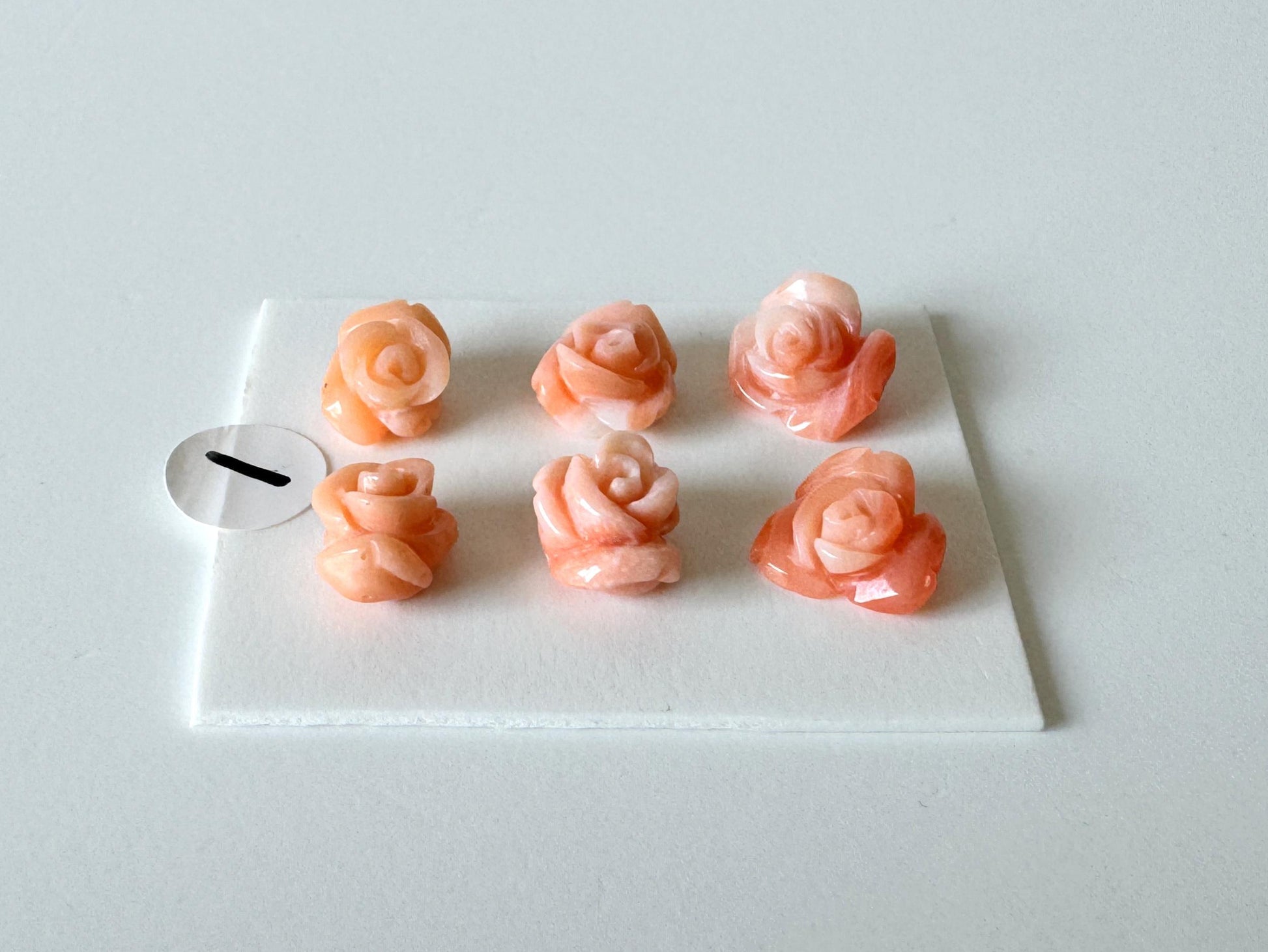 Six pink rose-shaped objects are arranged on a white surface, with one small white circle placed next to them.