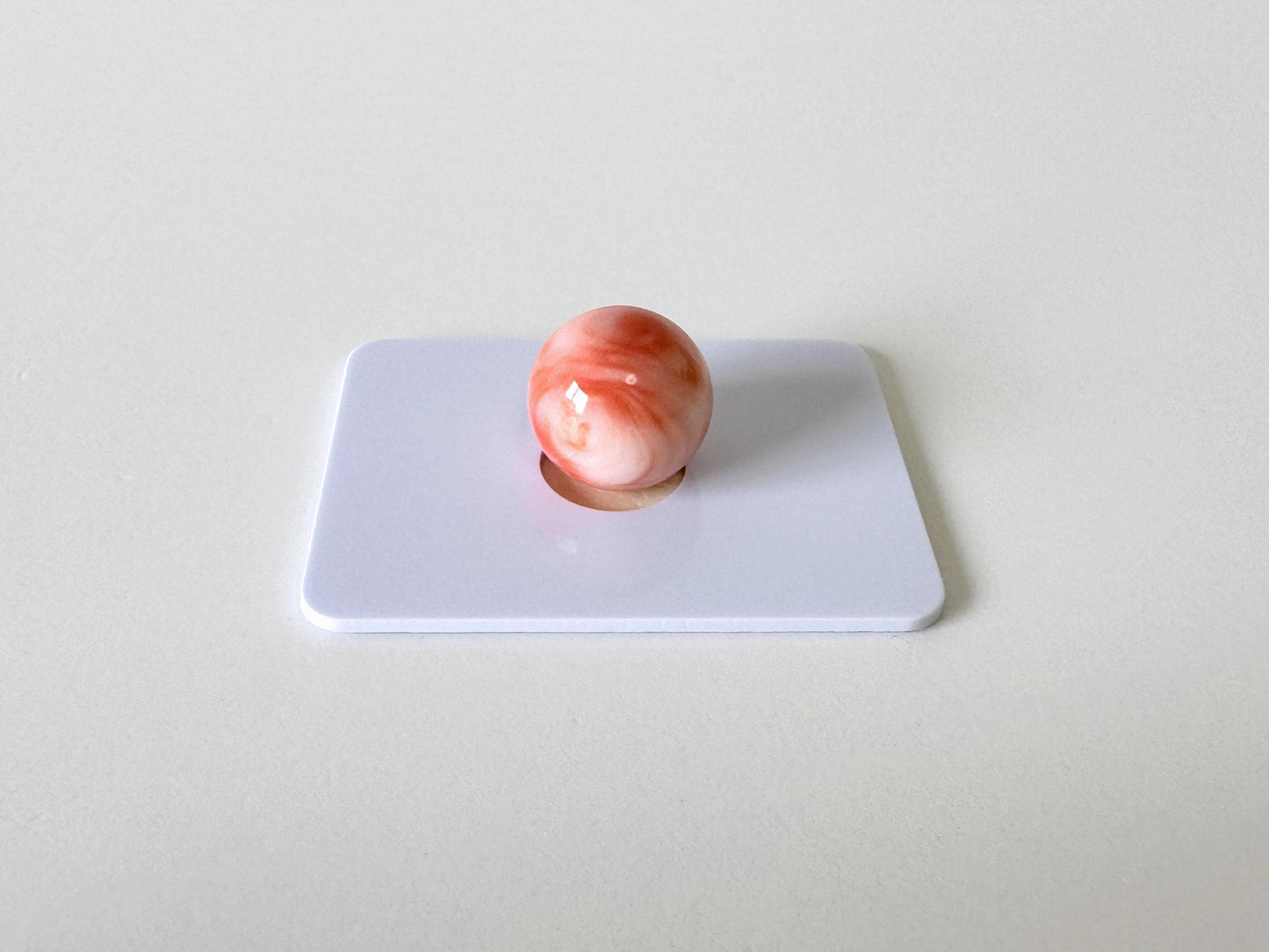 A single, round, red marble is resting on a white surface.