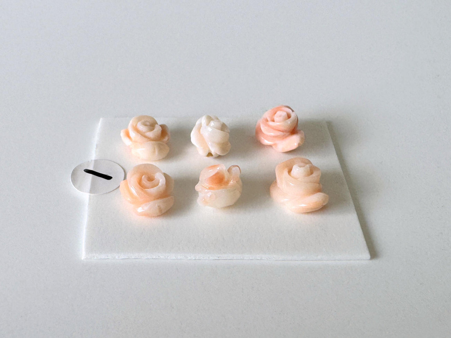 A white square plate with six small, delicate pink and white rose-shaped objects arranged neatly on it.