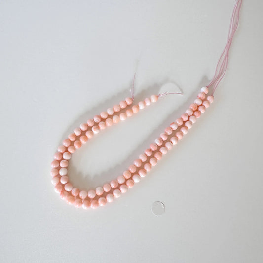 A necklace made of small, round beads in a soft pink color, with a small silver bead lying next to it on a plain white surface.