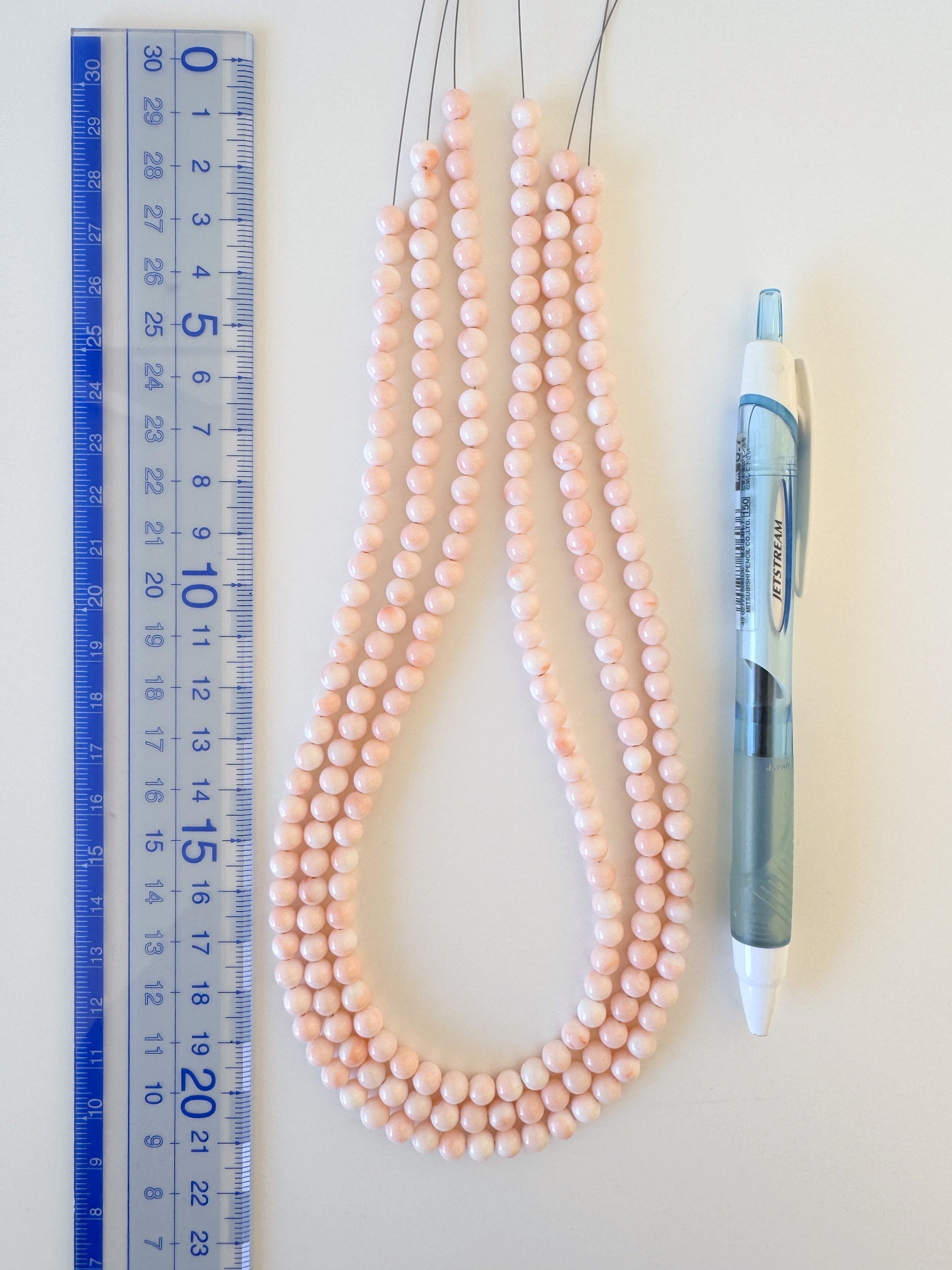 a collection of three beaded necklaces and a pen, with a ruler placed next to them.