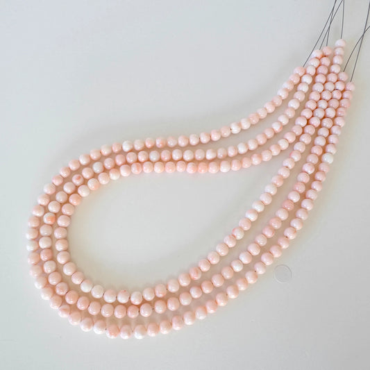 A necklace composed of numerous small, round beads in a light pink color, arranged in a curved pattern.