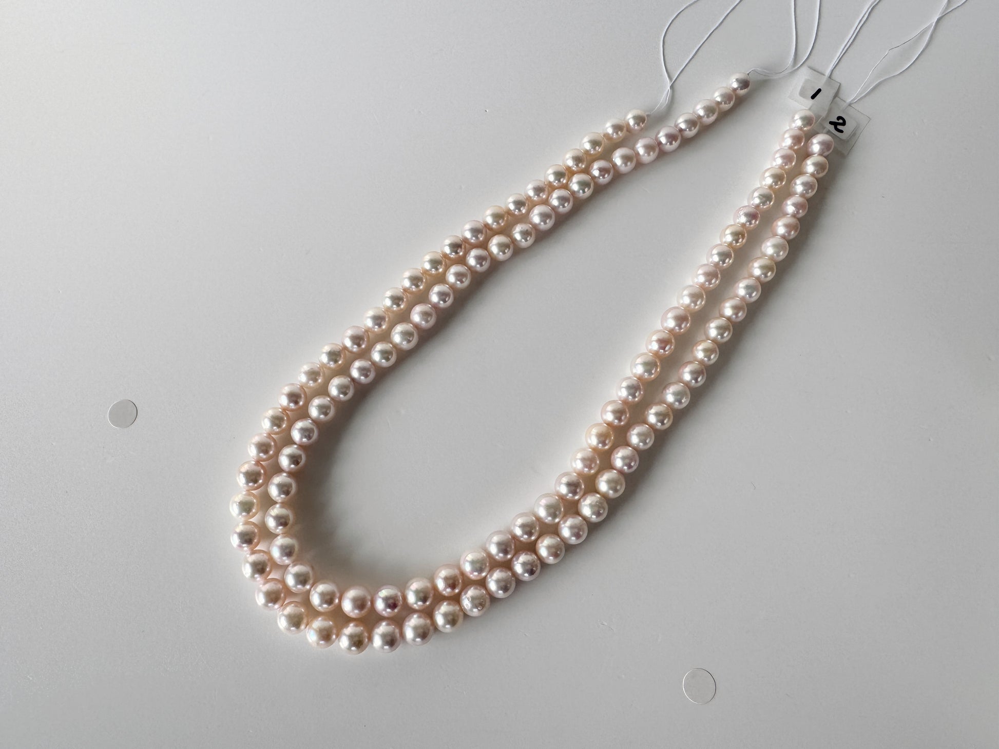 A necklace made of small, round, white pearls is displayed on a white surface.