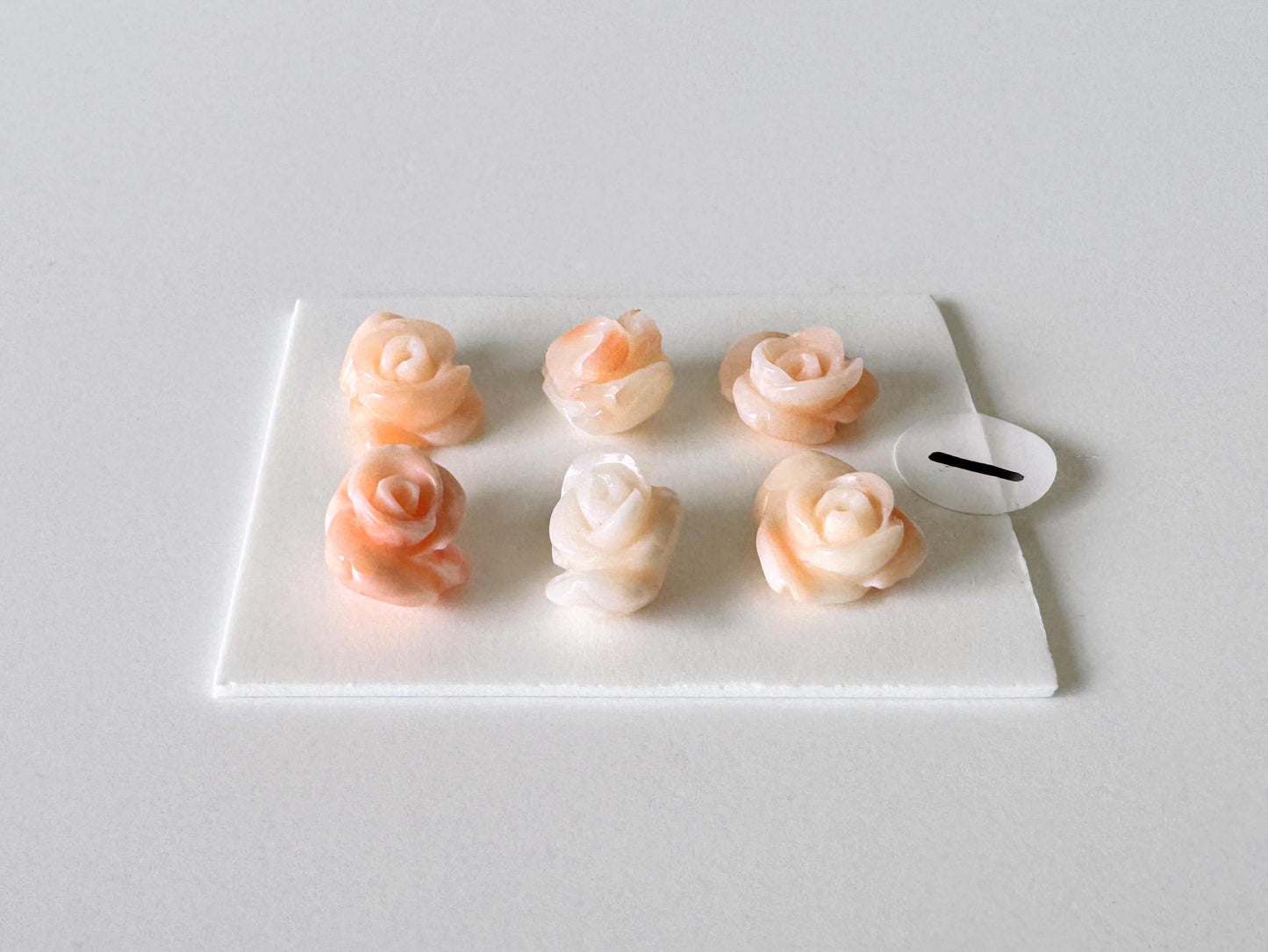 A white square plate with six small, delicate pink and white rose-shaped objects arranged in two rows of three.