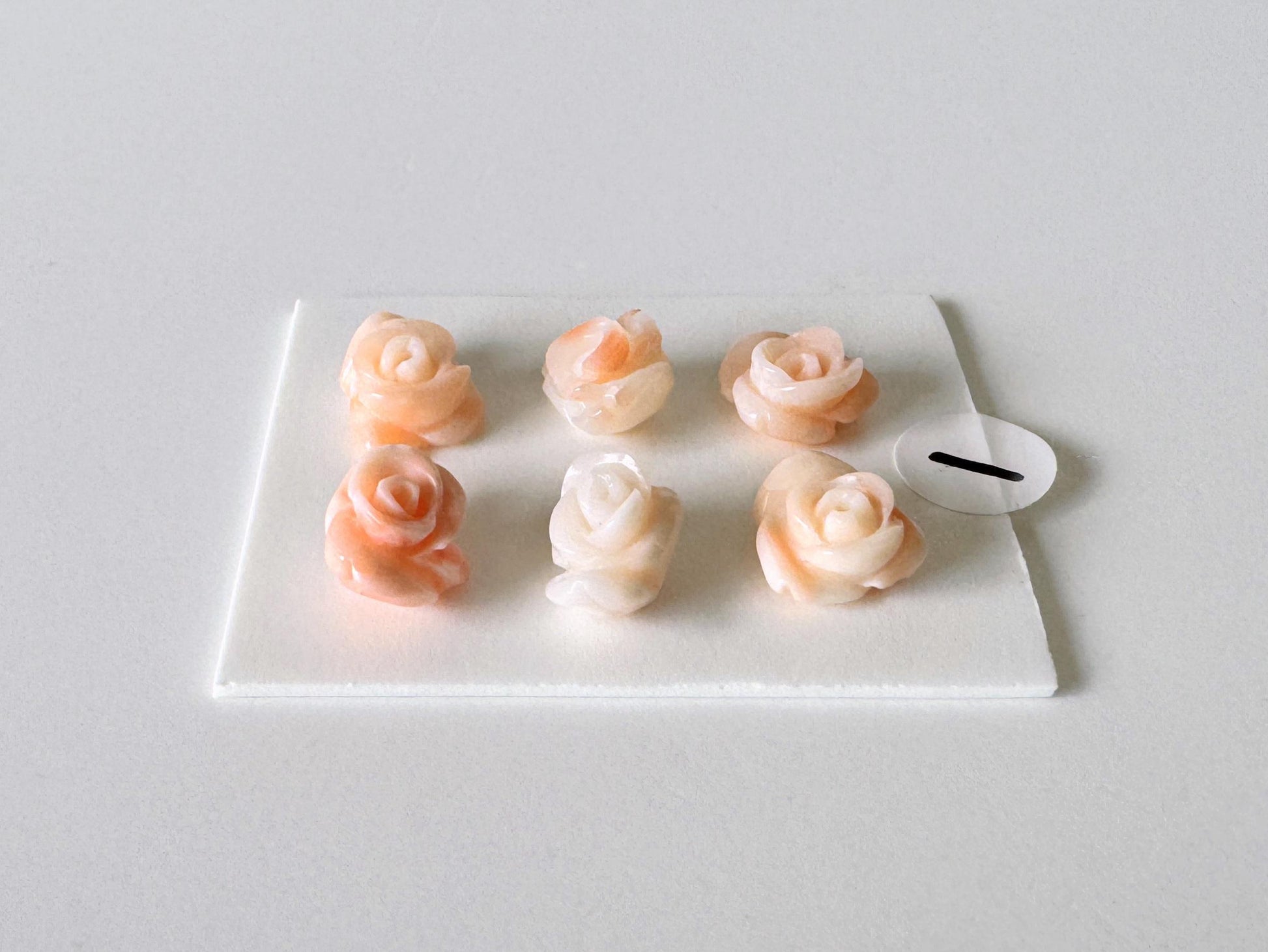 A white square plate with six small, delicate pink and white rose-shaped objects arranged in two rows of three.