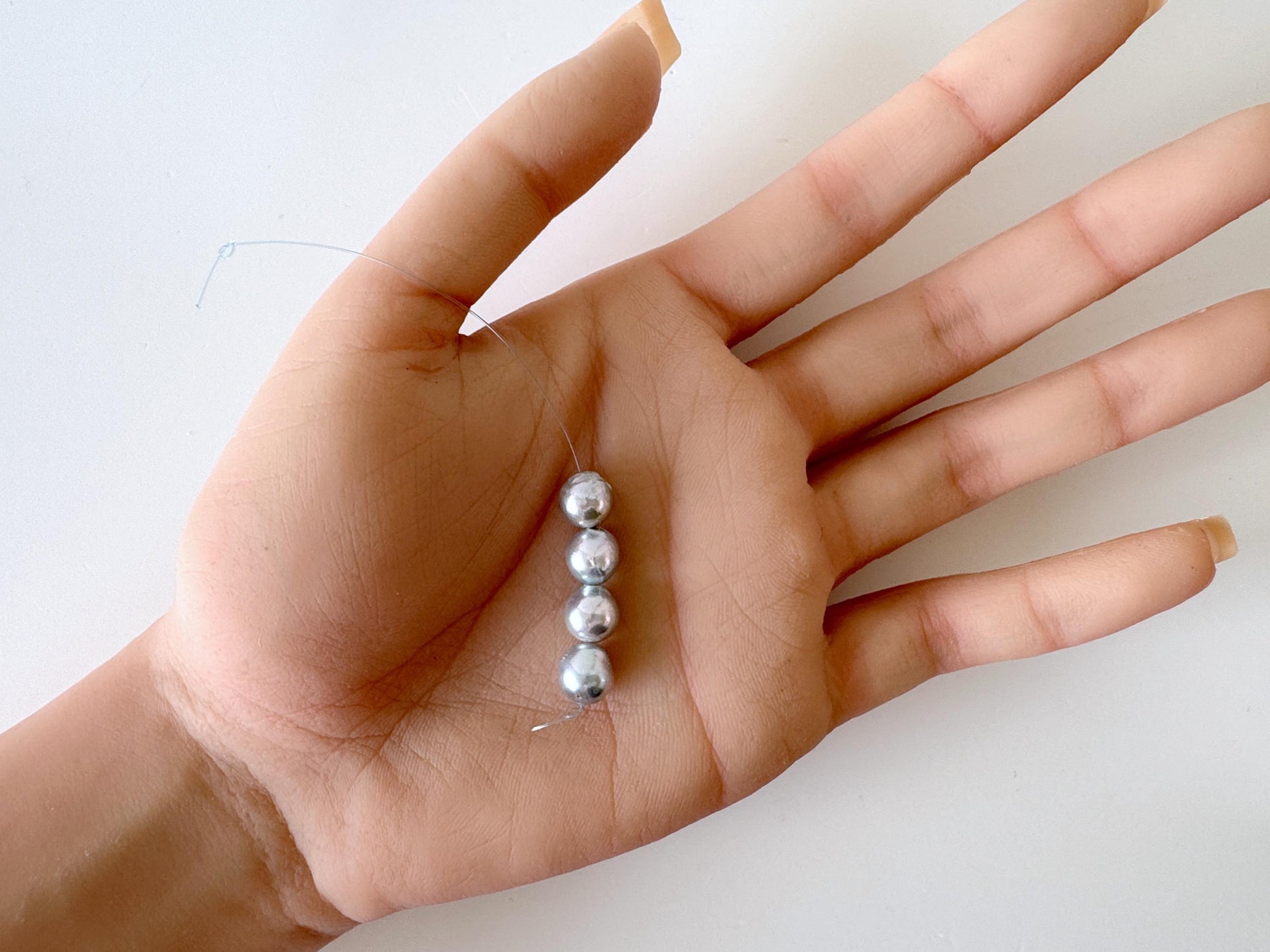 A hand holding a small group of silver beads.