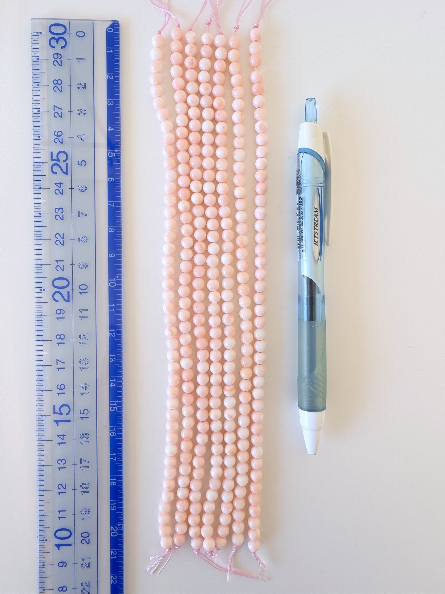 a collection of pink beads and a blue pen placed next to a ruler on a white surface.