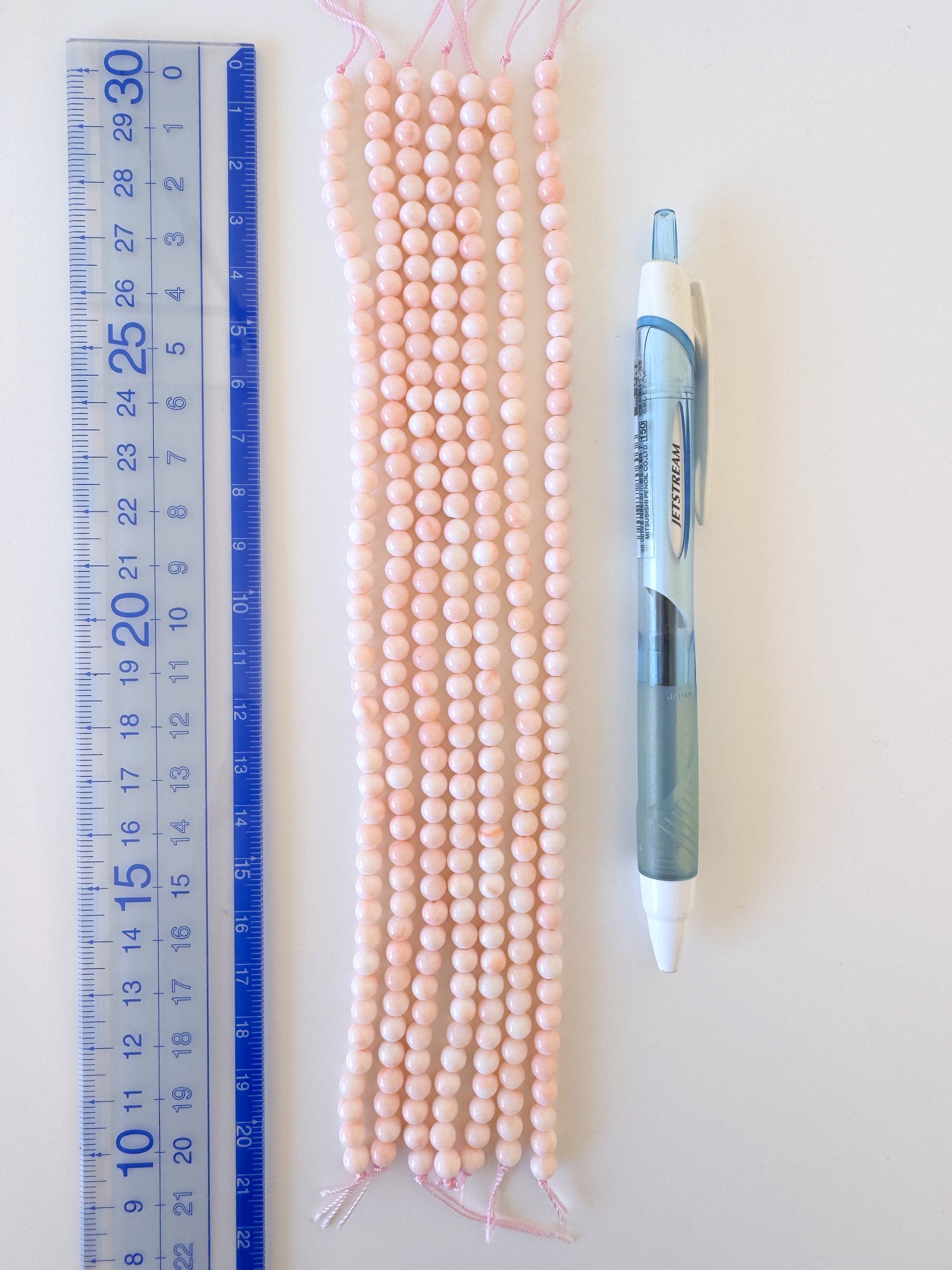 a collection of pink beads and a blue pen placed next to a ruler on a white surface.